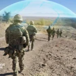 British soldier carrying a wearable electronic warfare jammer designed to counter drones and radio-frequency threats on the battlefield.